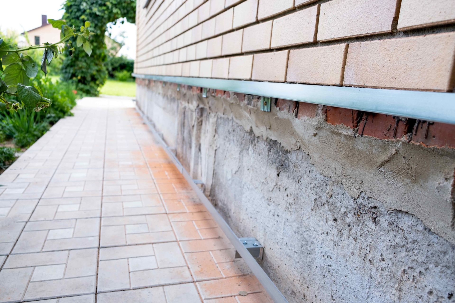 Brick building wall with visible foundation; light-colored tiled walkway.