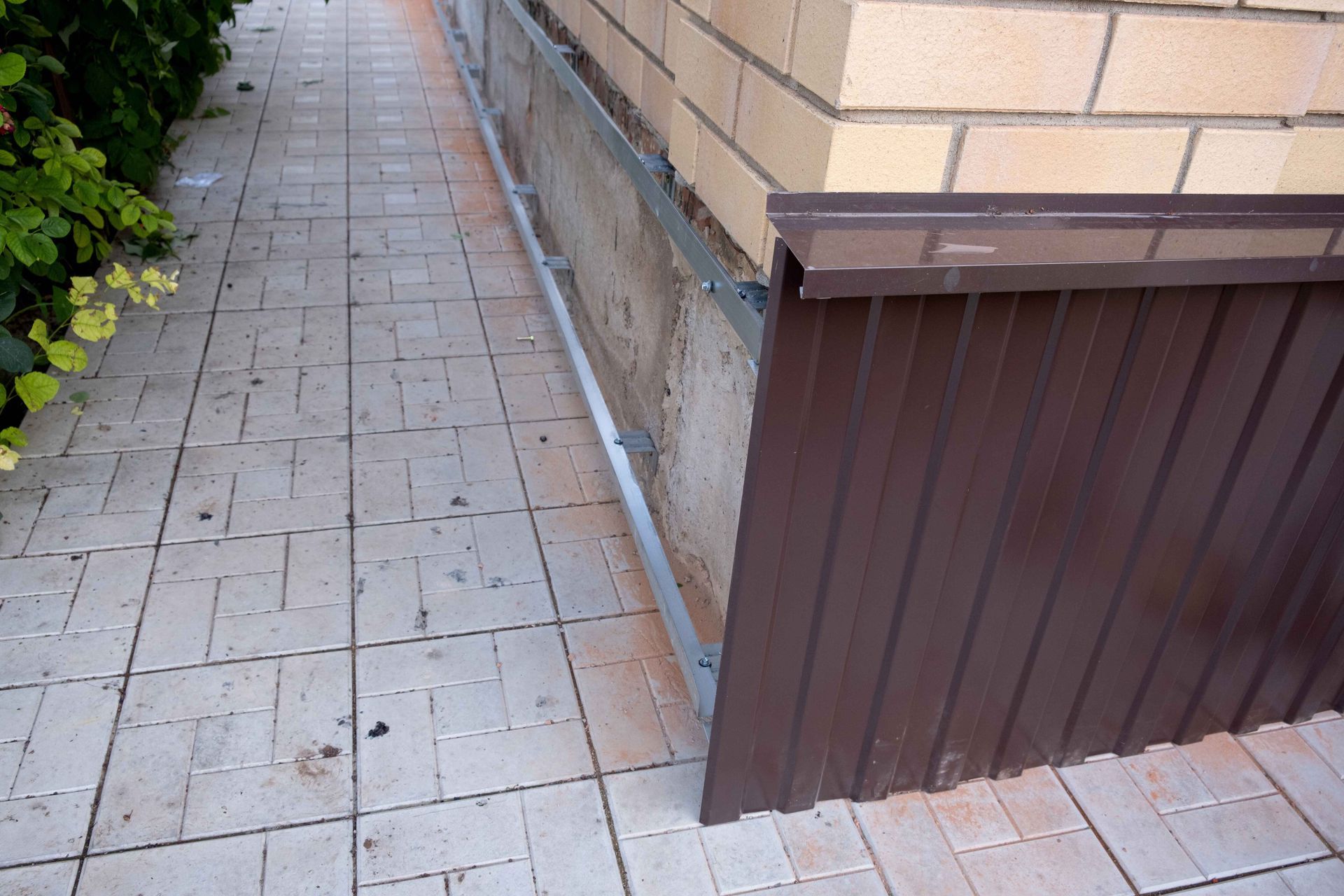 Brown corrugated metal siding installed on a brick building's foundation, next to tiled walkway.