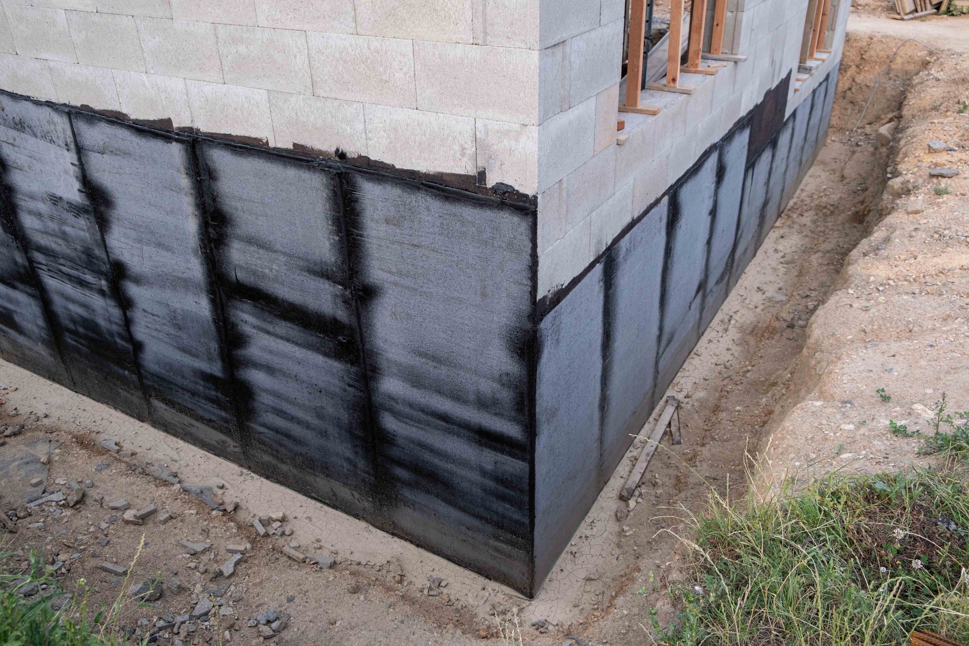 Foundation of a building with black waterproofing membrane applied, surrounded by excavated dirt.