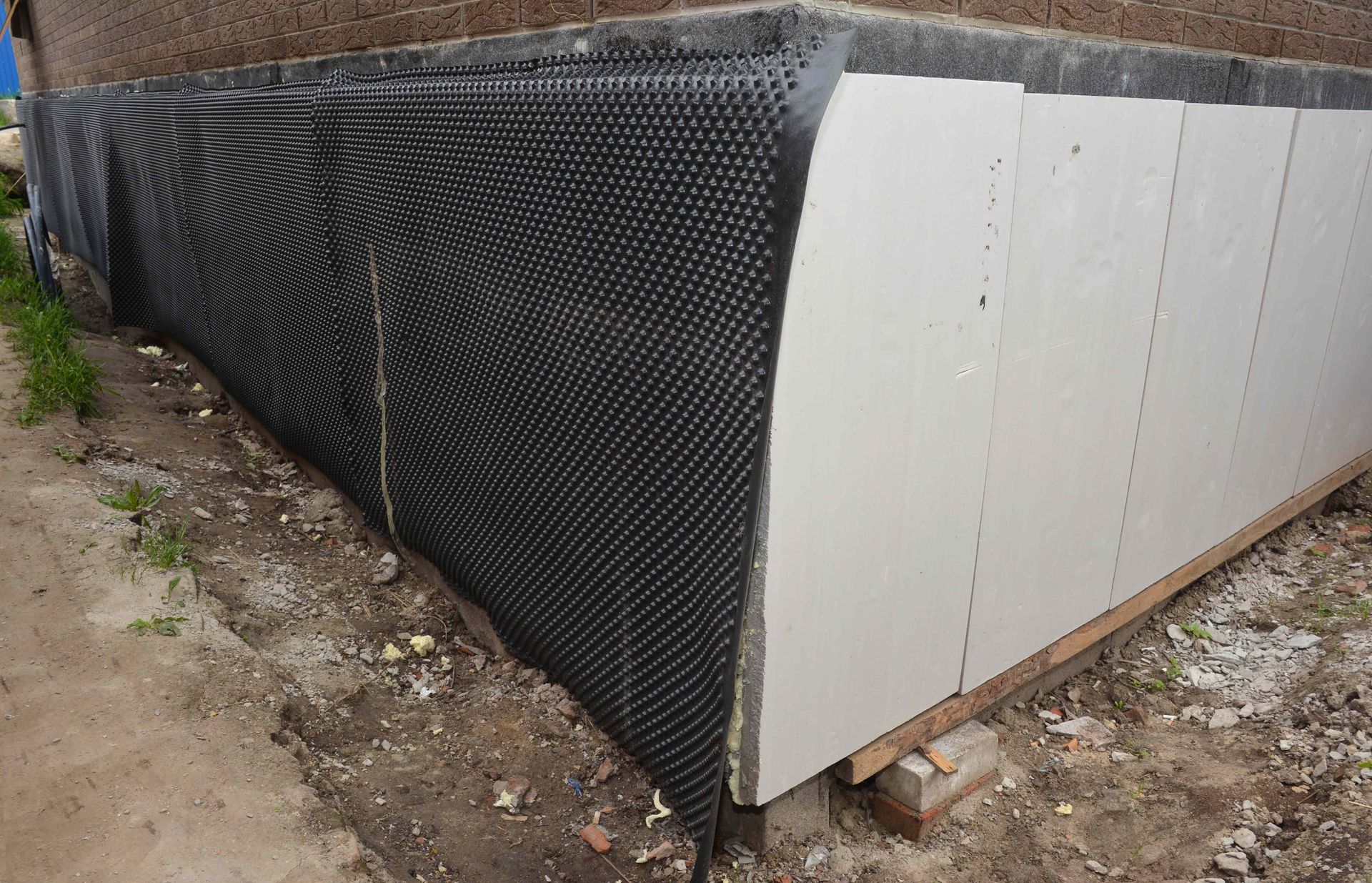 Foundation corner with black drainage membrane and white insulation panels.