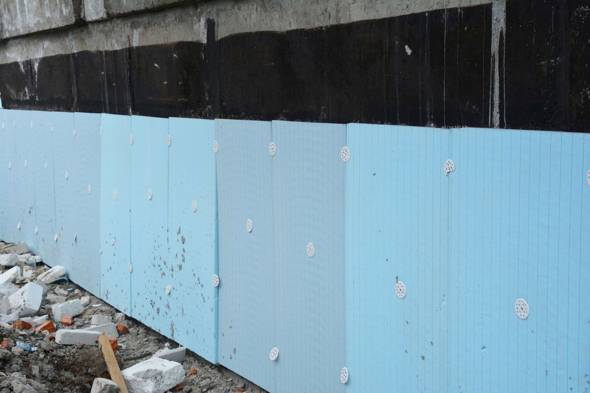 Blue foam insulation panels attached to a dark wall, with debris at the base.