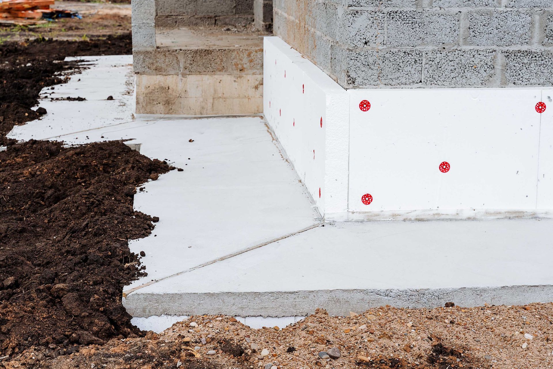 Foundation of a building under construction, with concrete and white insulation against cinder blocks and dirt.