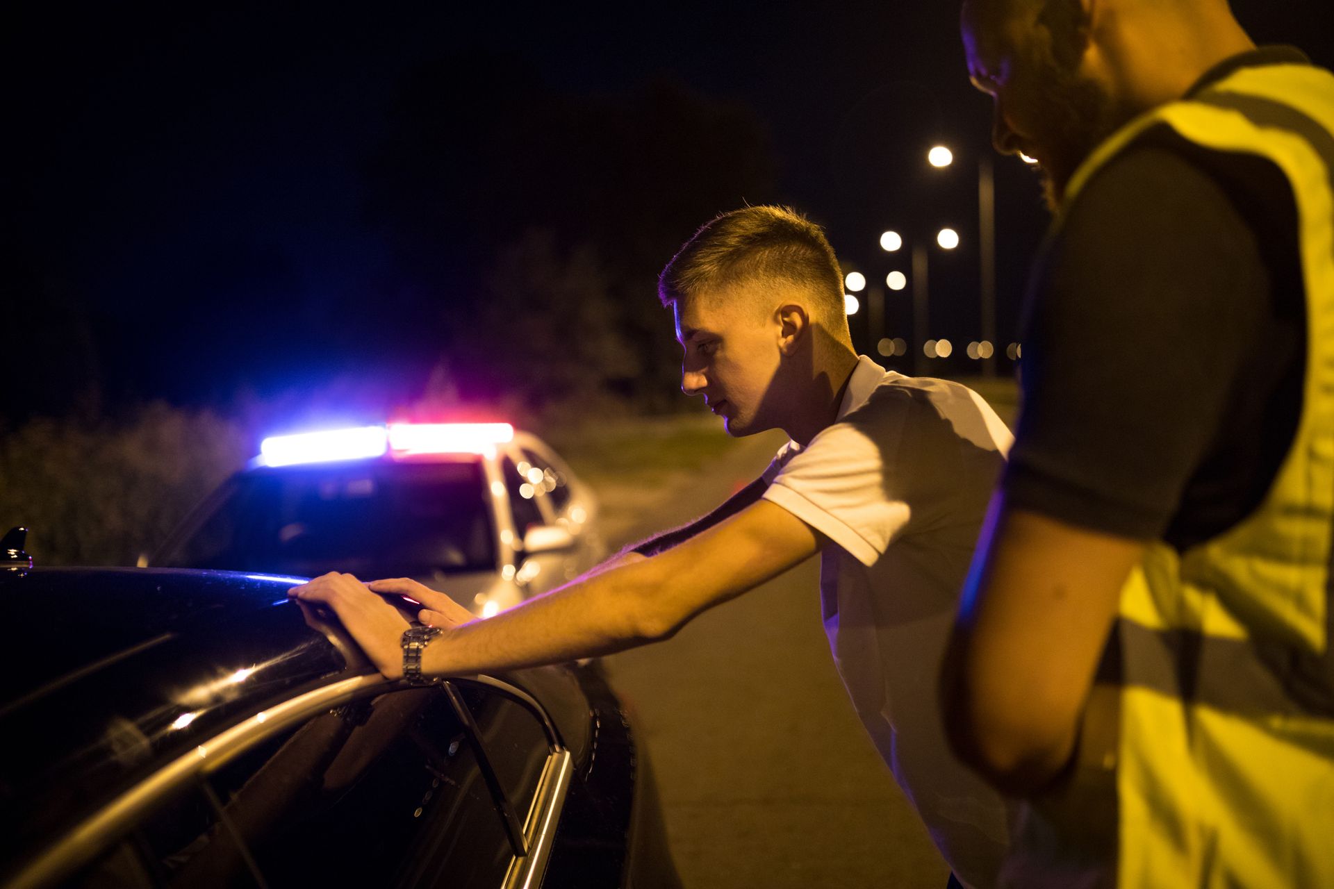 A man is getting out of a police car at night.