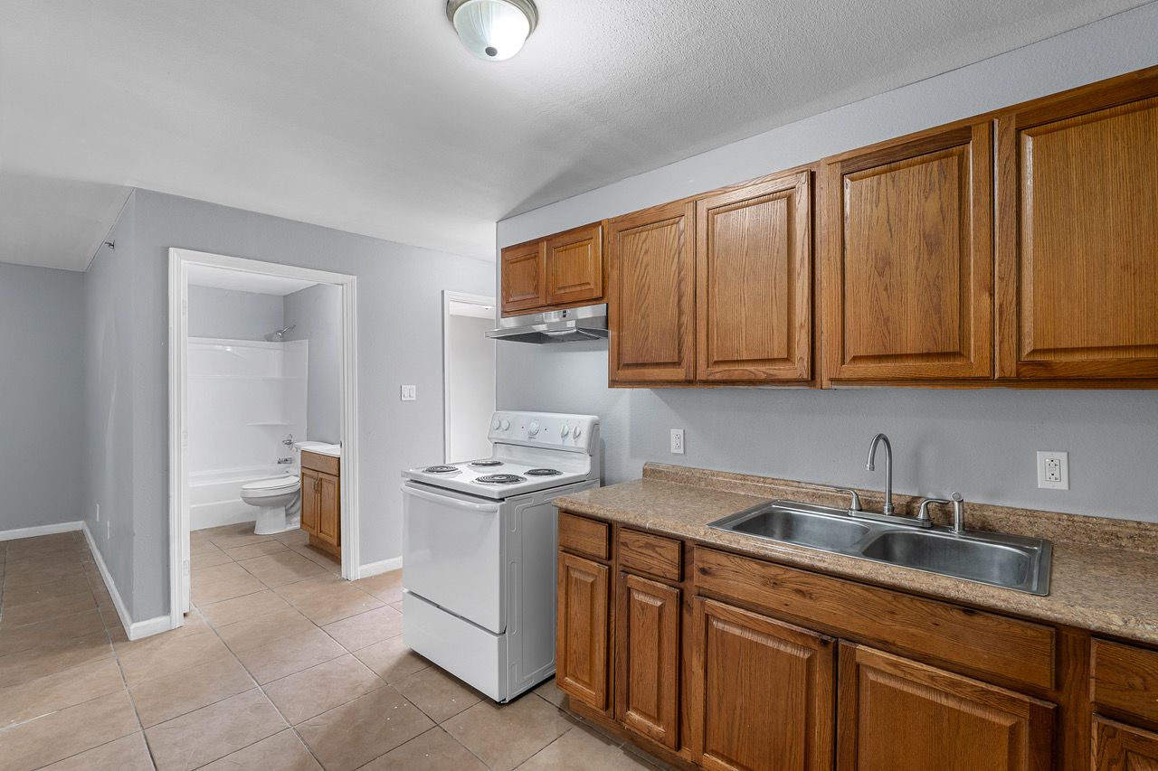 a kitchen with wooden cabinets , a stove , a sink and a toilet .