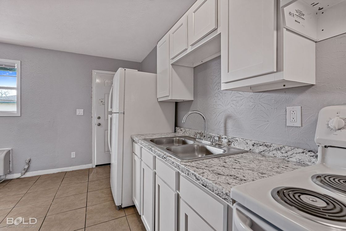 a kitchen with white cabinets , granite counter tops , a stove and a refrigerator .
