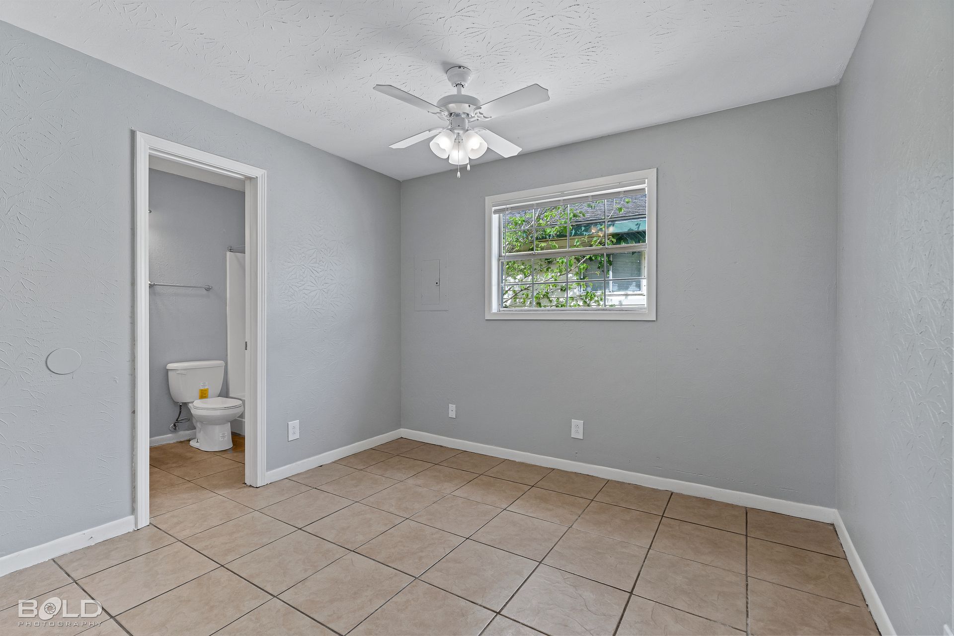 an empty bedroom with a ceiling fan and a toilet .
