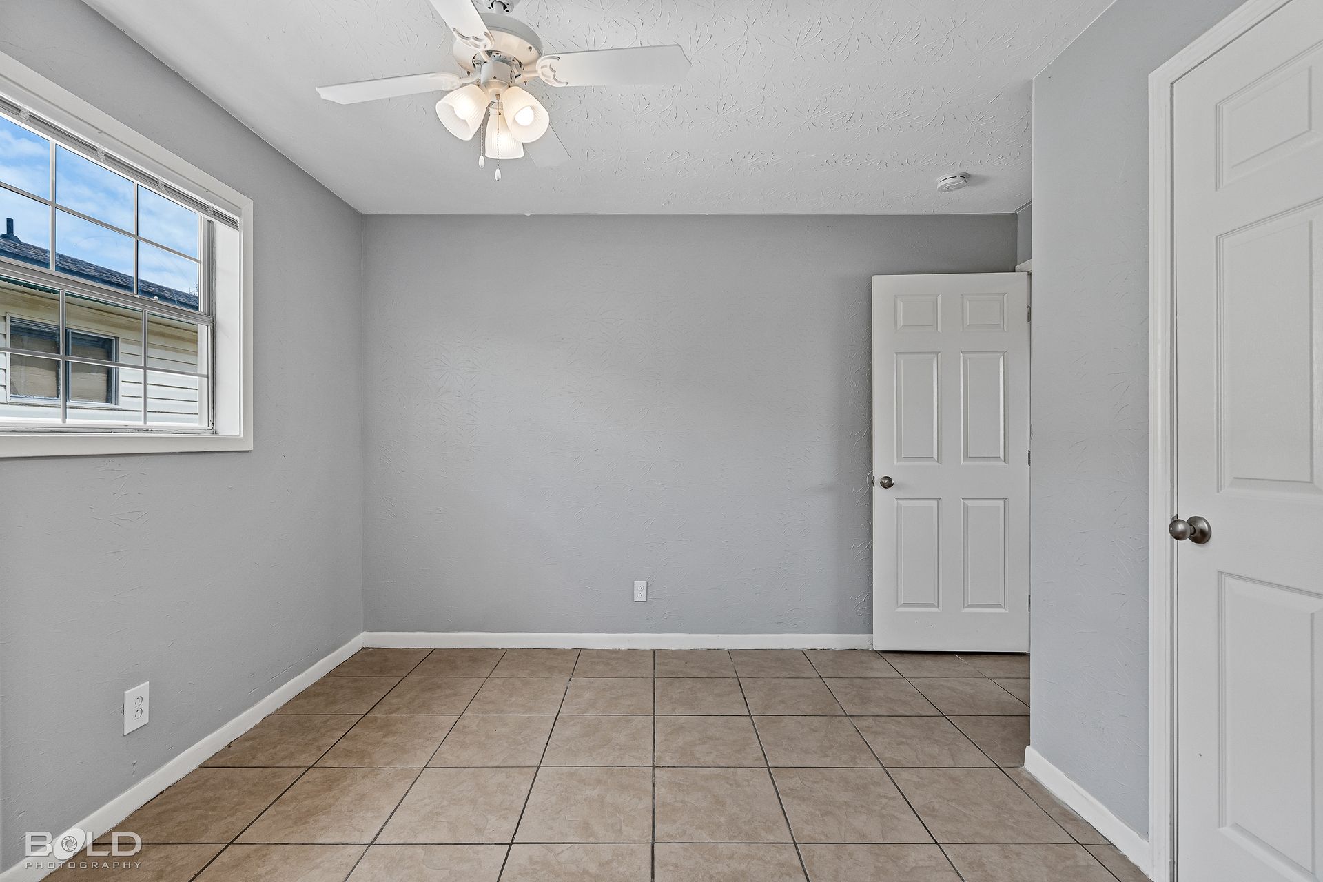 an empty bedroom with a ceiling fan and a window .