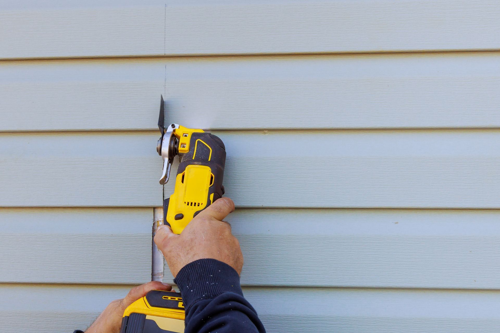 A contractor cutting a vinyl siding panel with a yellow cordless power tool A contractor cutting a vinyl siding panel with a yellow cordless power tool