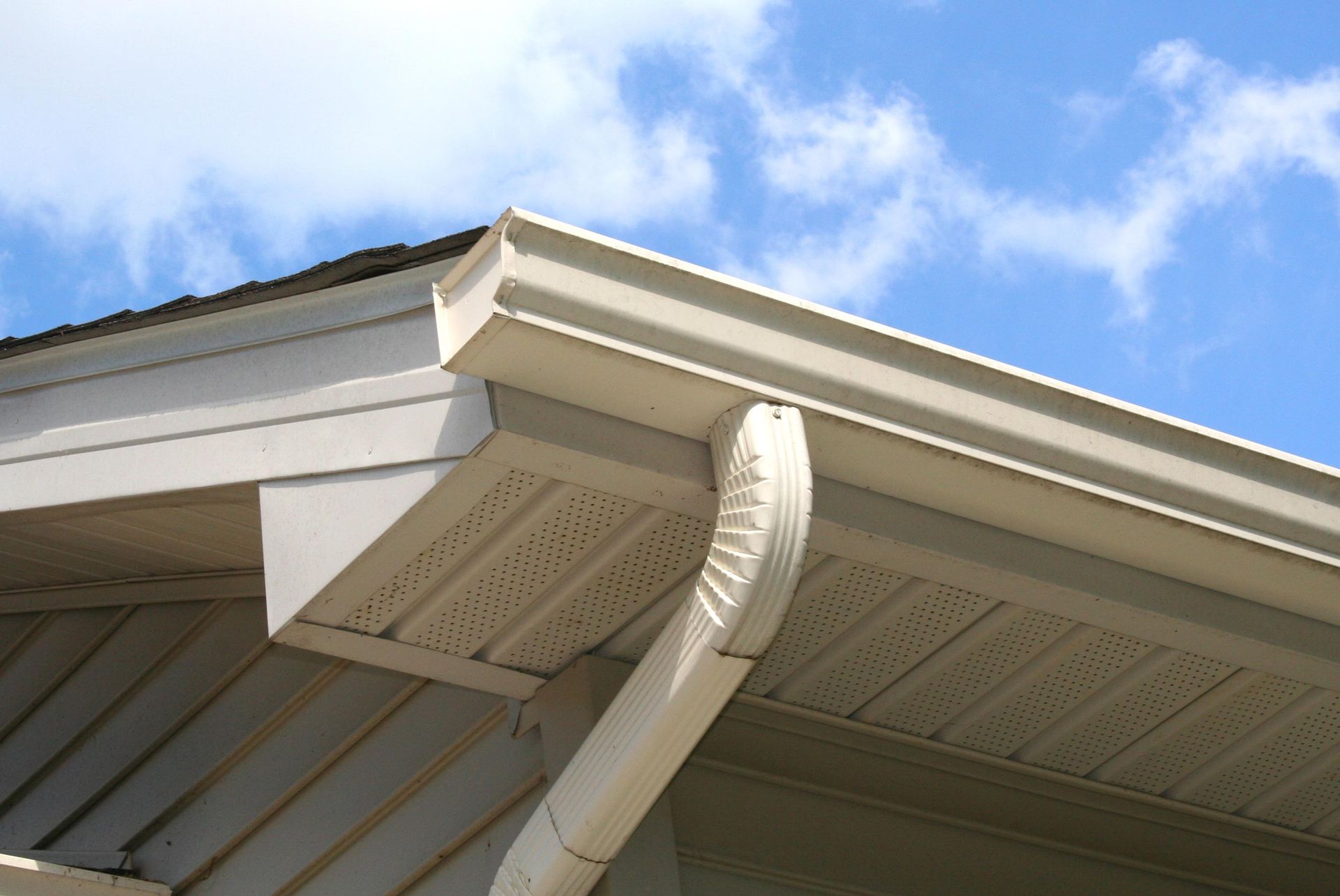 A white gutter on the side of a house with a blue sky in the background