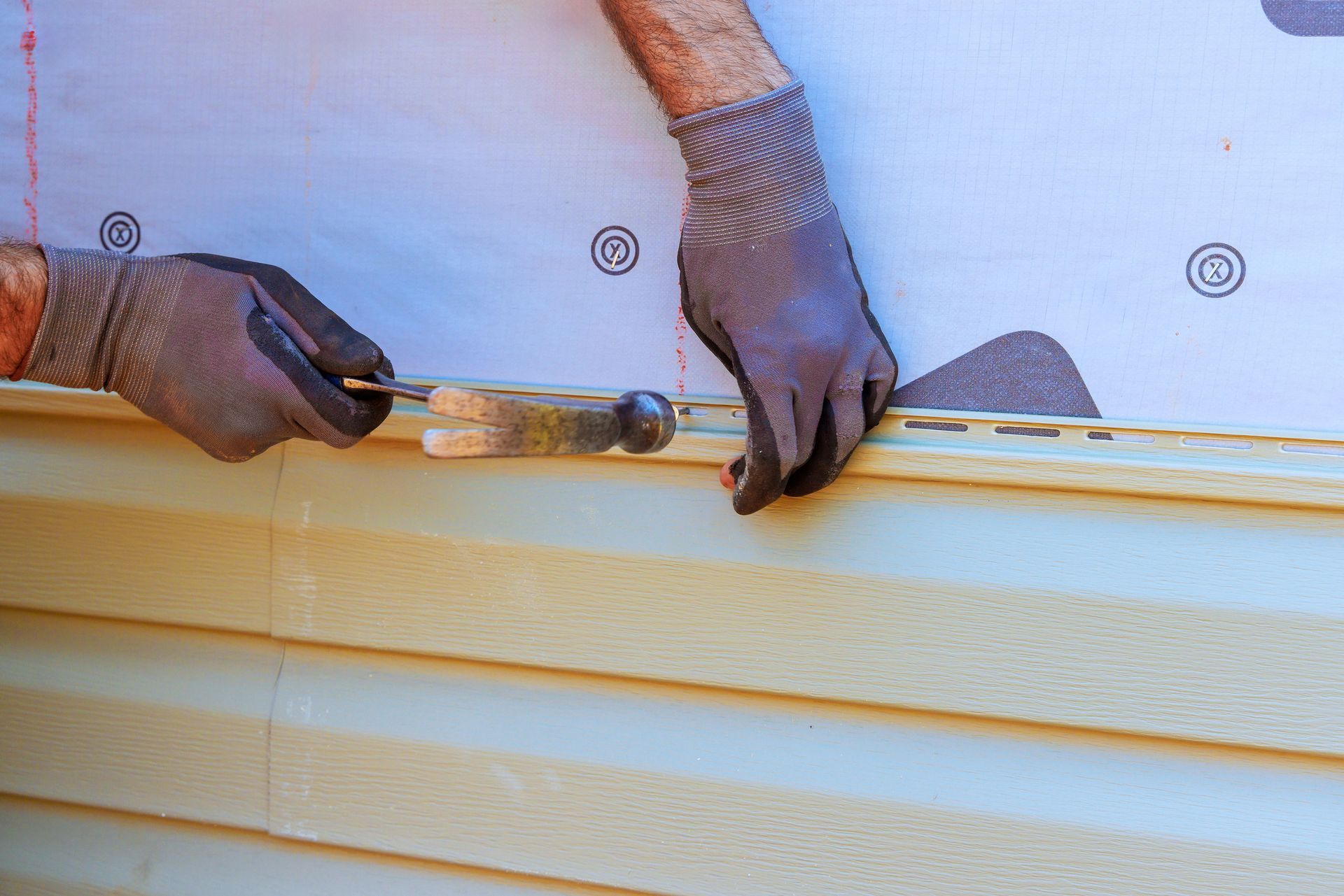 A worker is installing vinyl siding on a house.