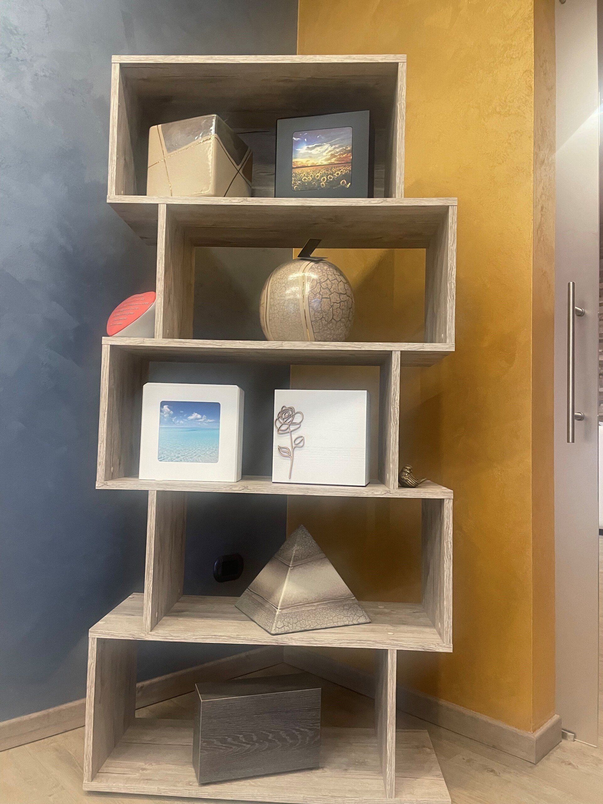 Mensola marrone chiaro a zig-zag con vari oggetti decorativi su pareti blu e gialle.