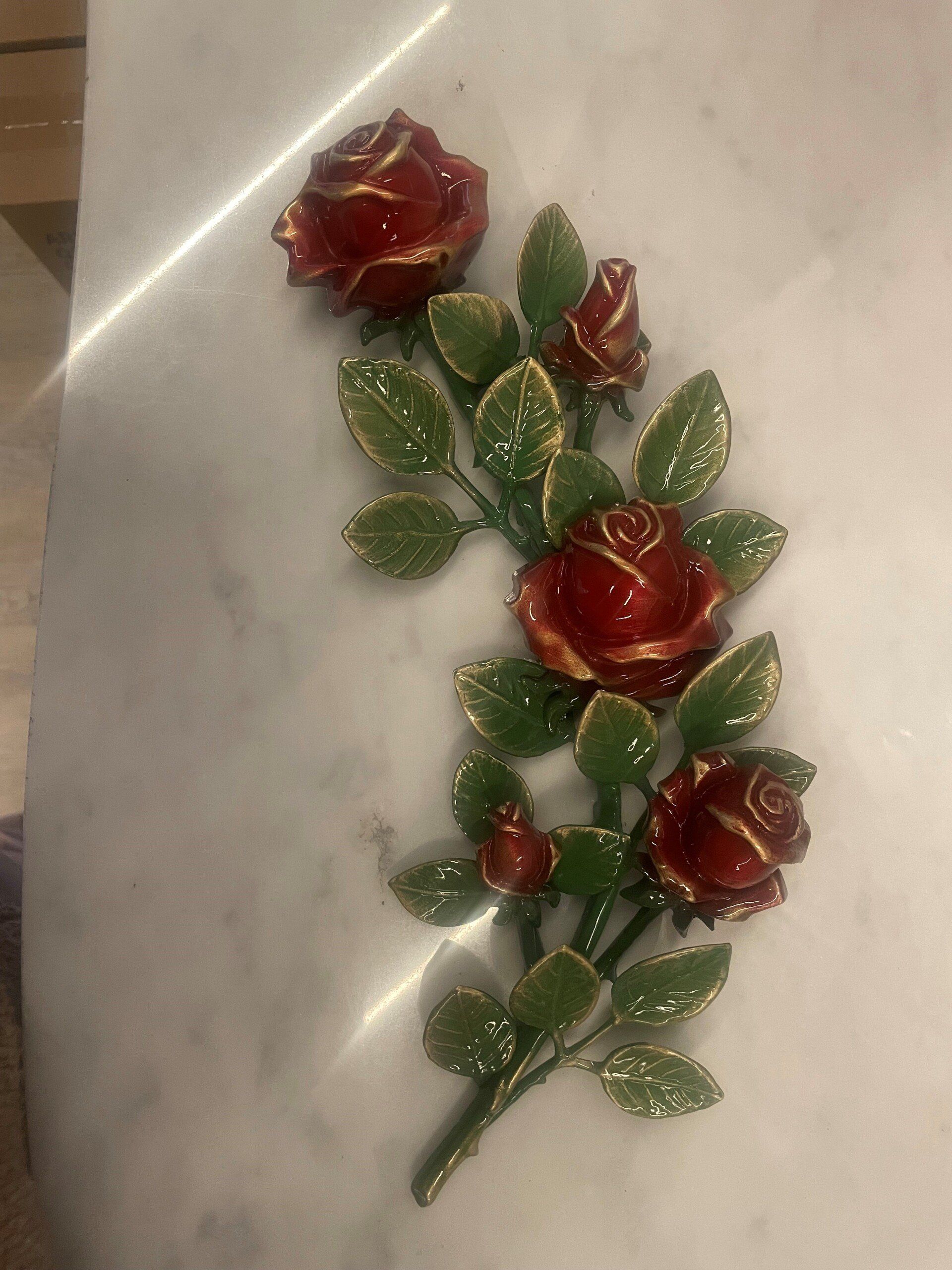 Rose rosse con finiture dorate e foglie verdi, disposte su una superficie di marmo bianco.