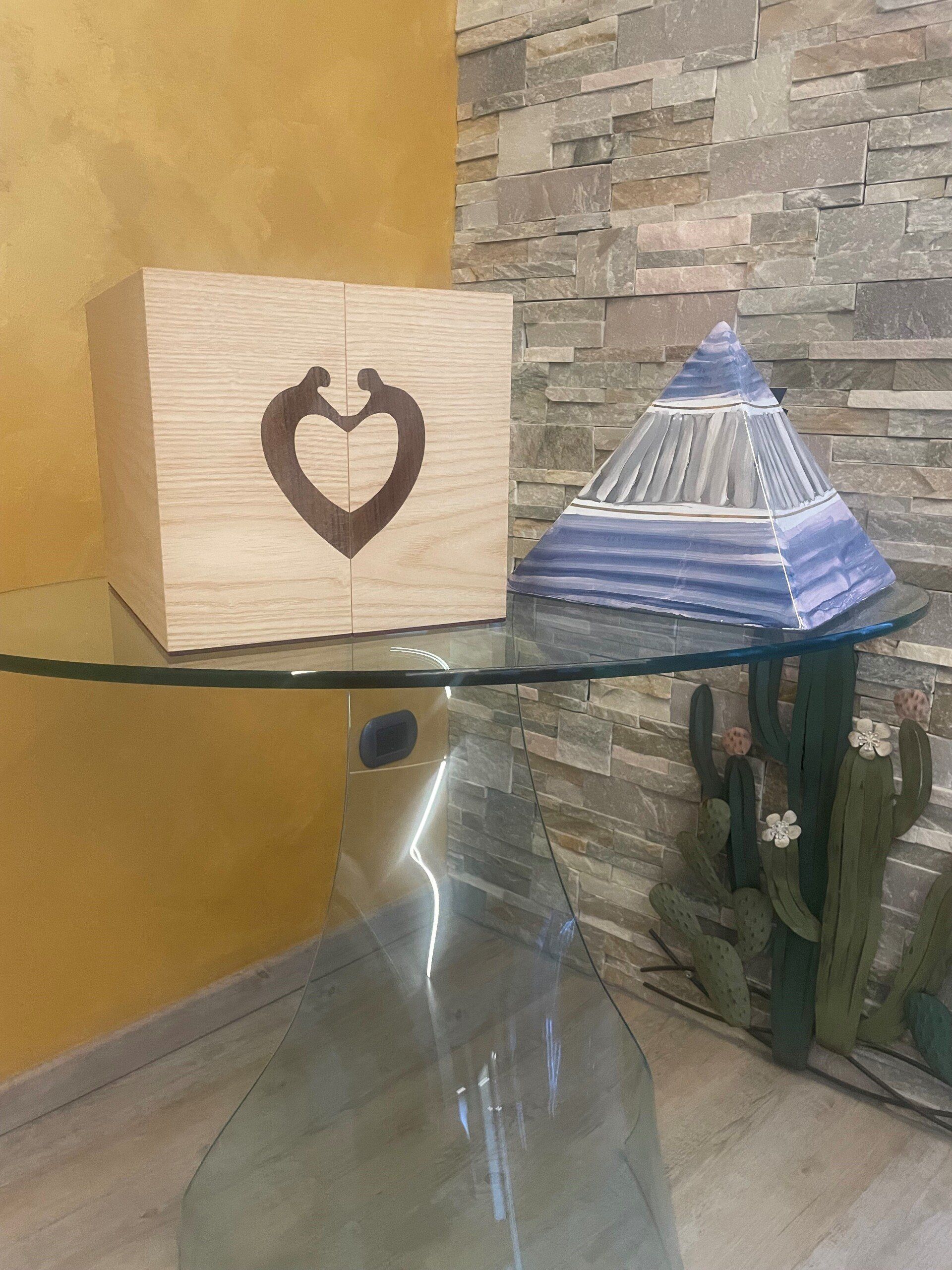 Scatola di legno con motivo a cuore e oggetto a forma di piramide su un tavolo di vetro.