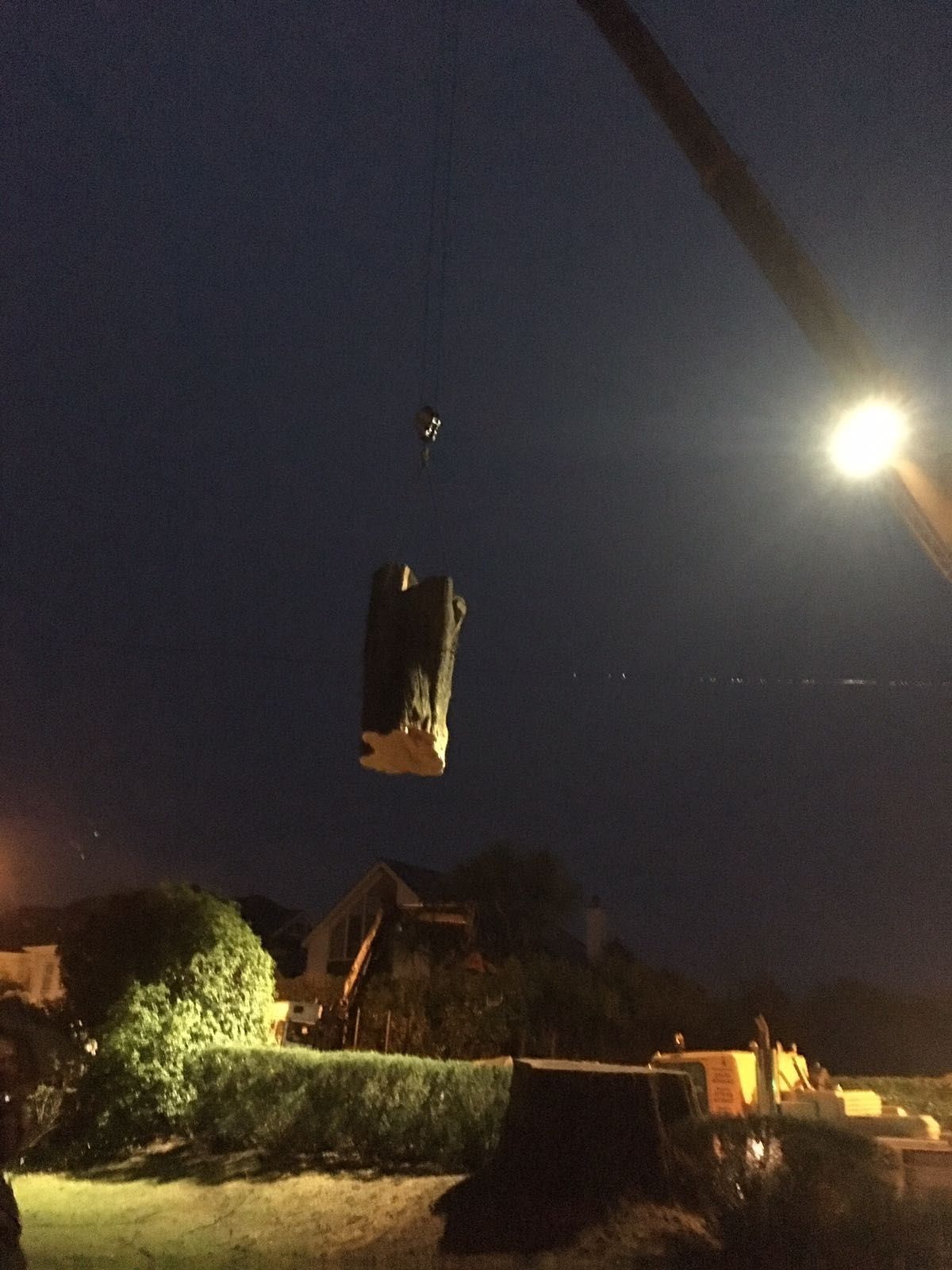 A large piece of wood is being lifted by a crane at night