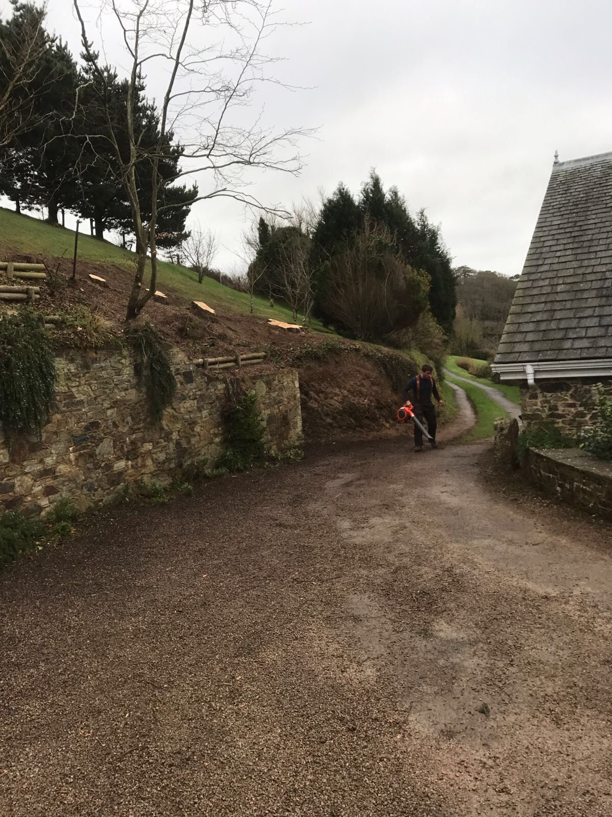 A person is walking down a dirt road next to a stone wall.