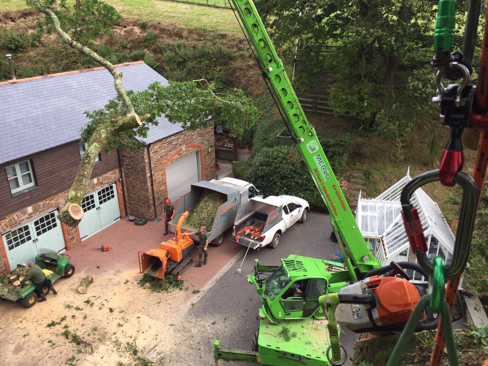 A green crane is cutting a tree in front of a house.