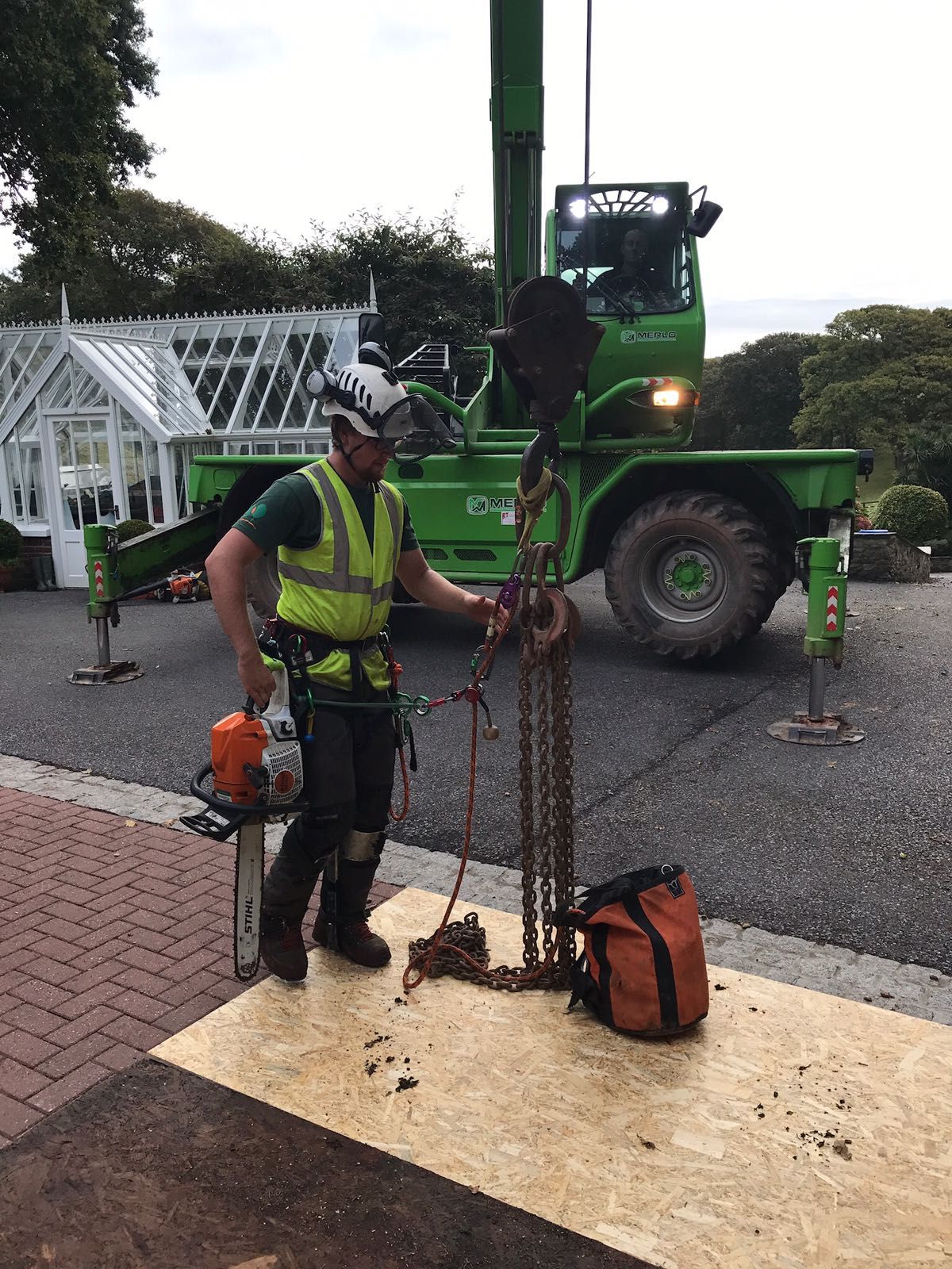 A man is standing in front of a green crane holding a chainsaw.