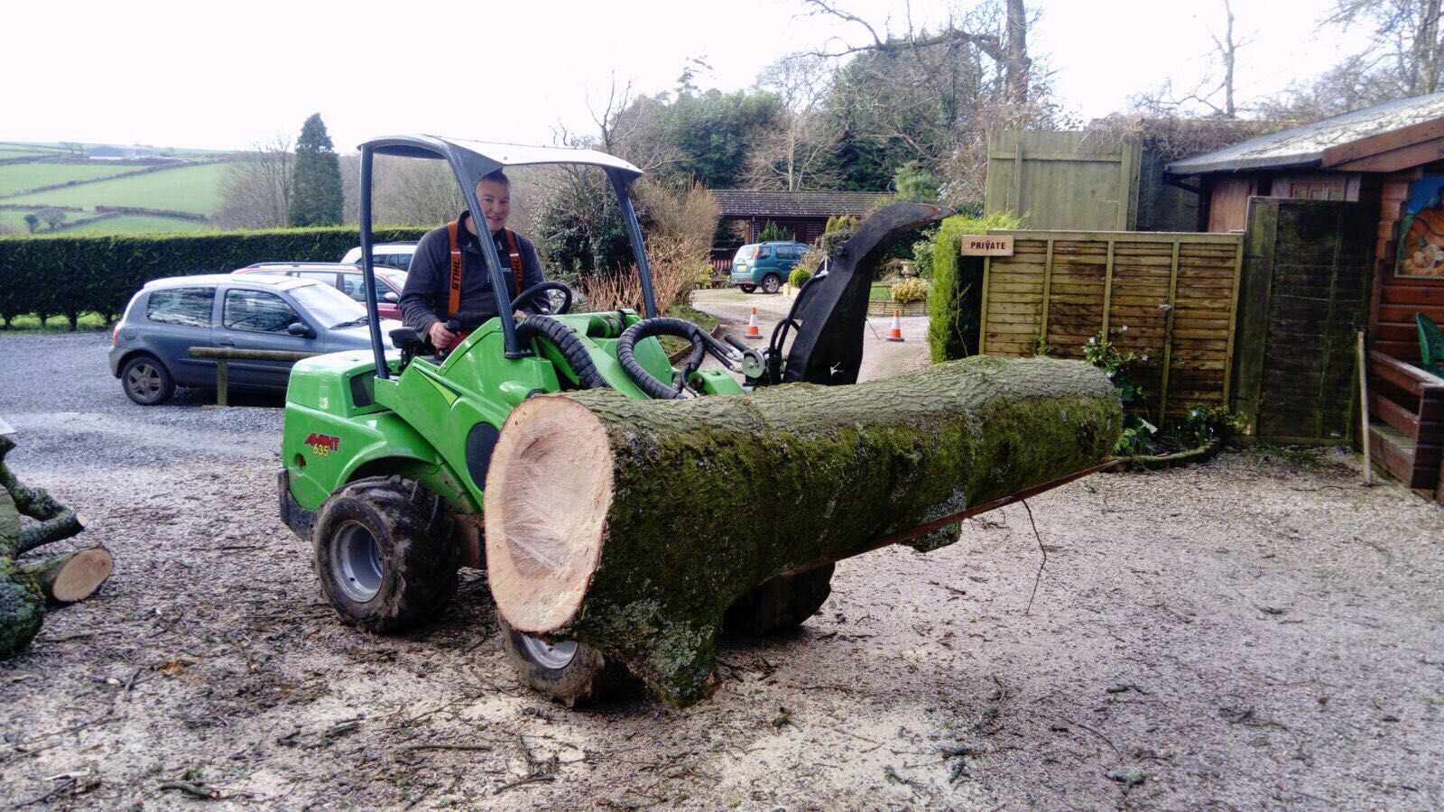A man is driving a green tractor with a large log on it.