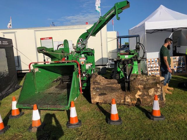 A green machine is sitting in the grass next to a pile of logs.