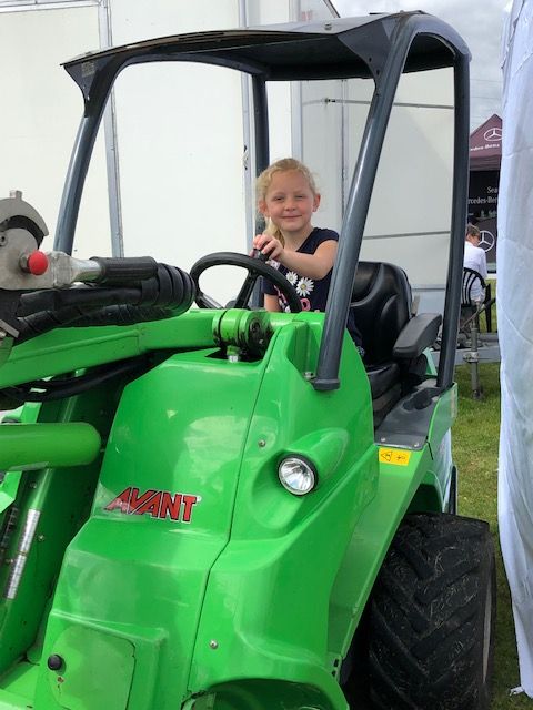 A little girl is sitting in a green tractor that says avant