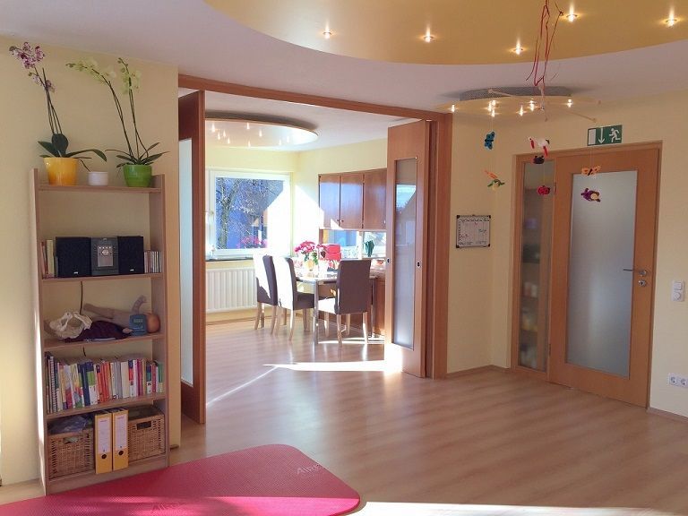 Heller Raum der Praxis mit warmen Farben, dunkelrot und orange mit Holz hauptsächlich.