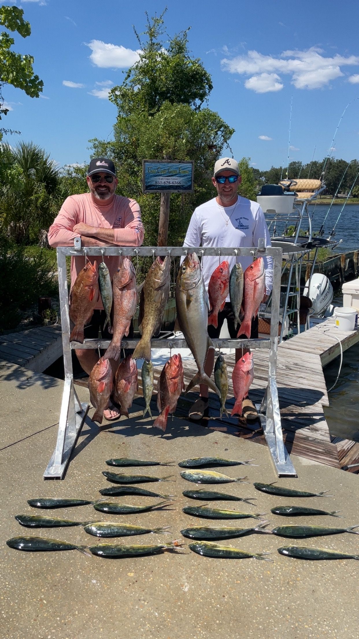 Two men pose with a large catch of fish on a pier, sunny day.