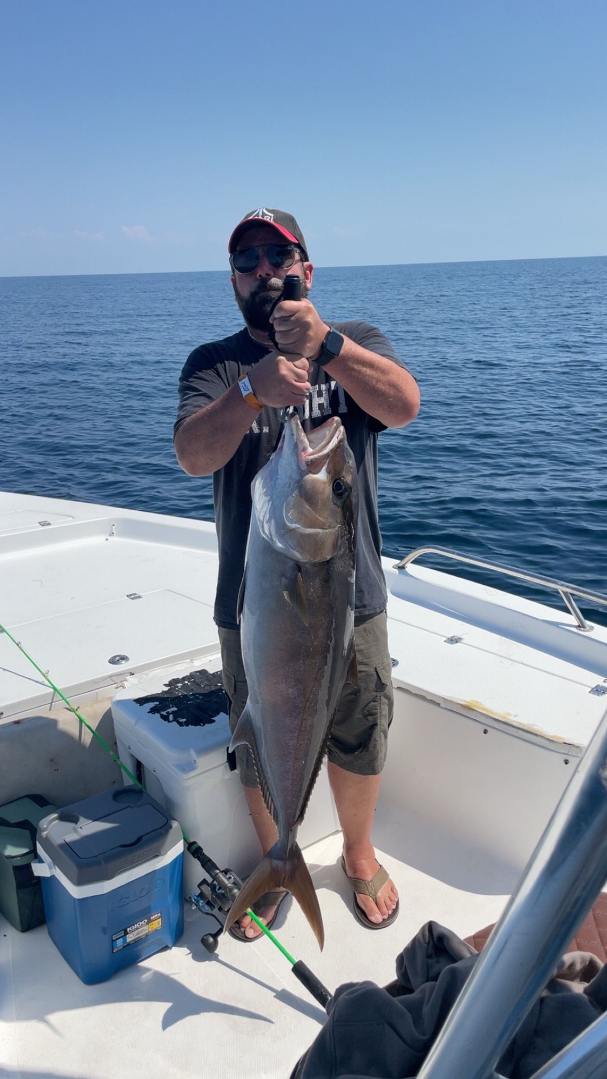 Man on a boat holding a large fish. Blue water and sky in the background.
