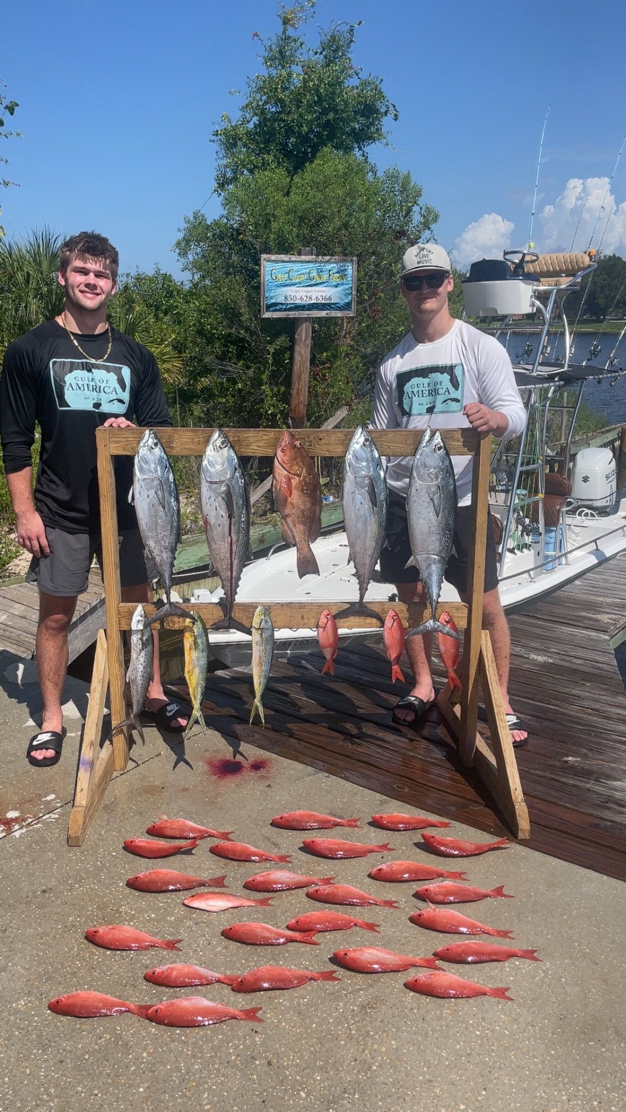 Two men with a fishing haul of red fish and other catches, on a pier.