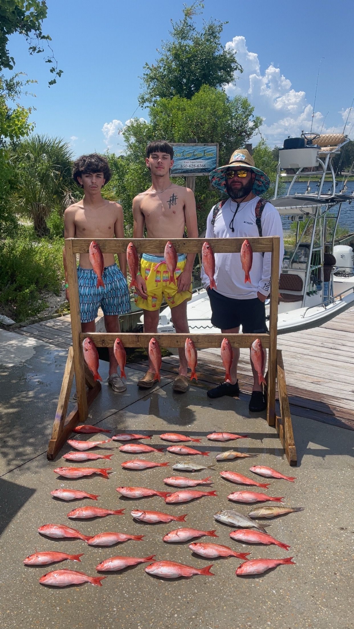 Three people proudly display a large catch of red fish after a fishing trip.