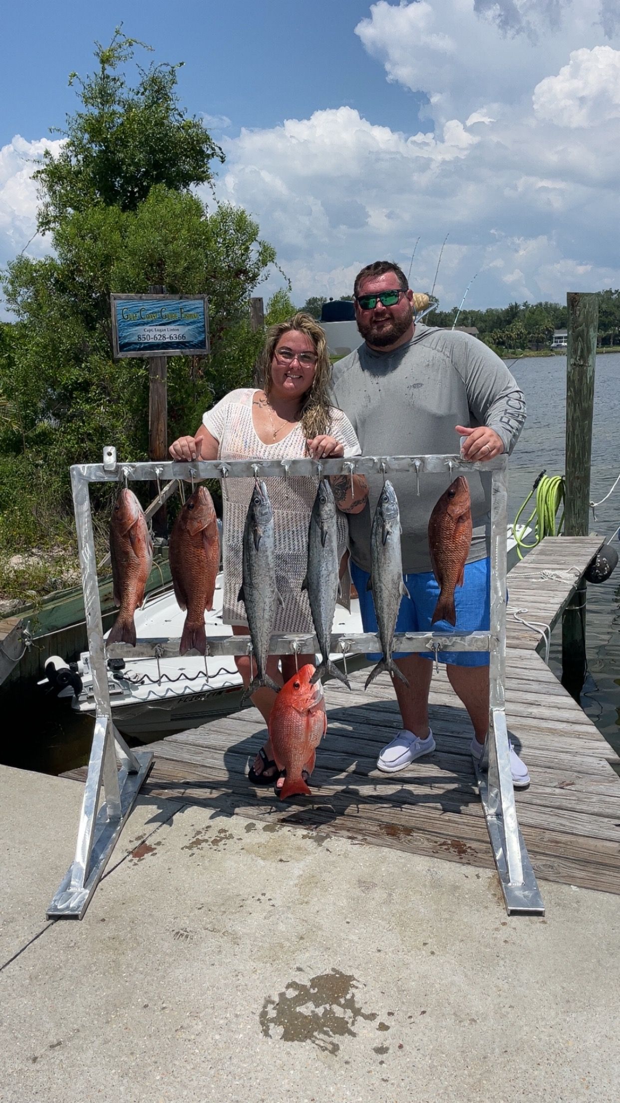 Two people posing with their catch of fish on a pier, sunny day.