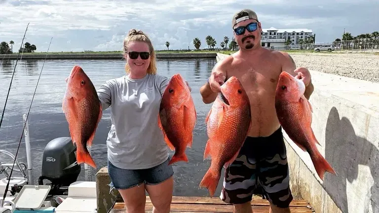 A man and a woman are holding two large red fish on a dock.