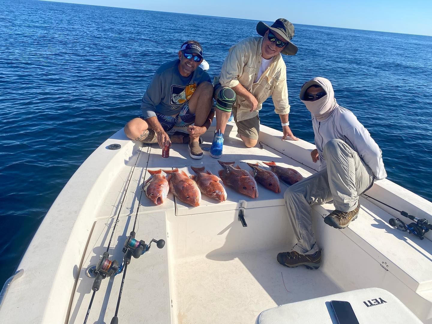 Three men are sitting on a boat with fish on the deck.