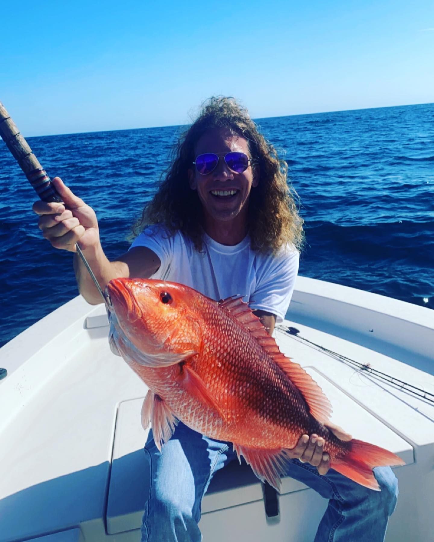 A man is sitting on a boat holding a large red fish