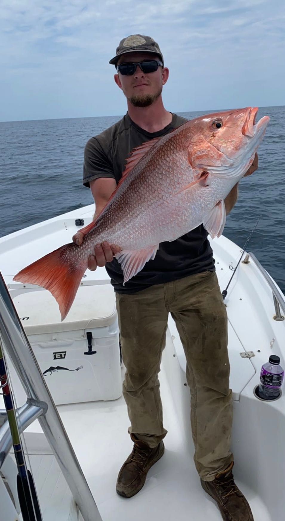 A man is standing on a boat holding a large red fish.