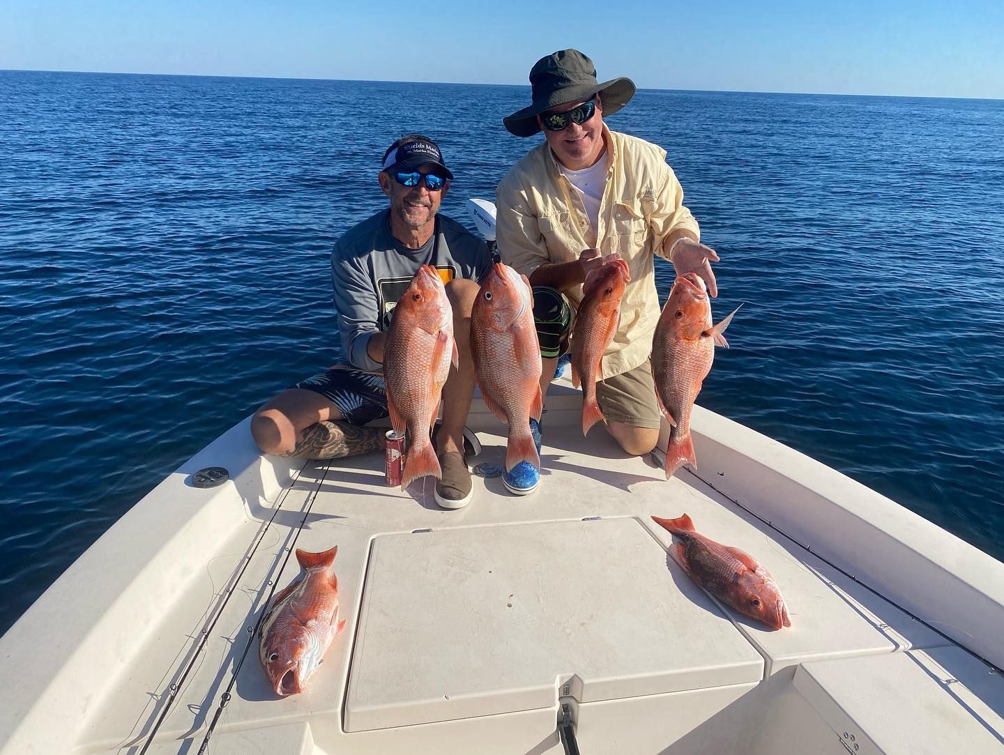 Two men are sitting on the back of a boat holding fish.