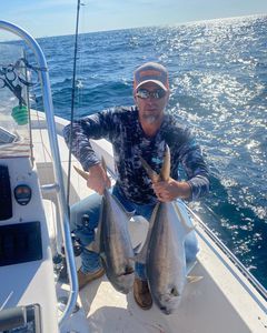A man is sitting on a boat holding two fish.