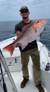A man is standing on a boat holding a large red fish.