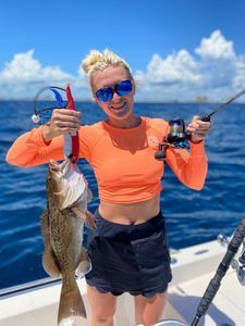 A woman is holding a fish and a fishing rod on a boat.
