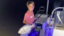 A young boy is standing on a boat holding two fish.