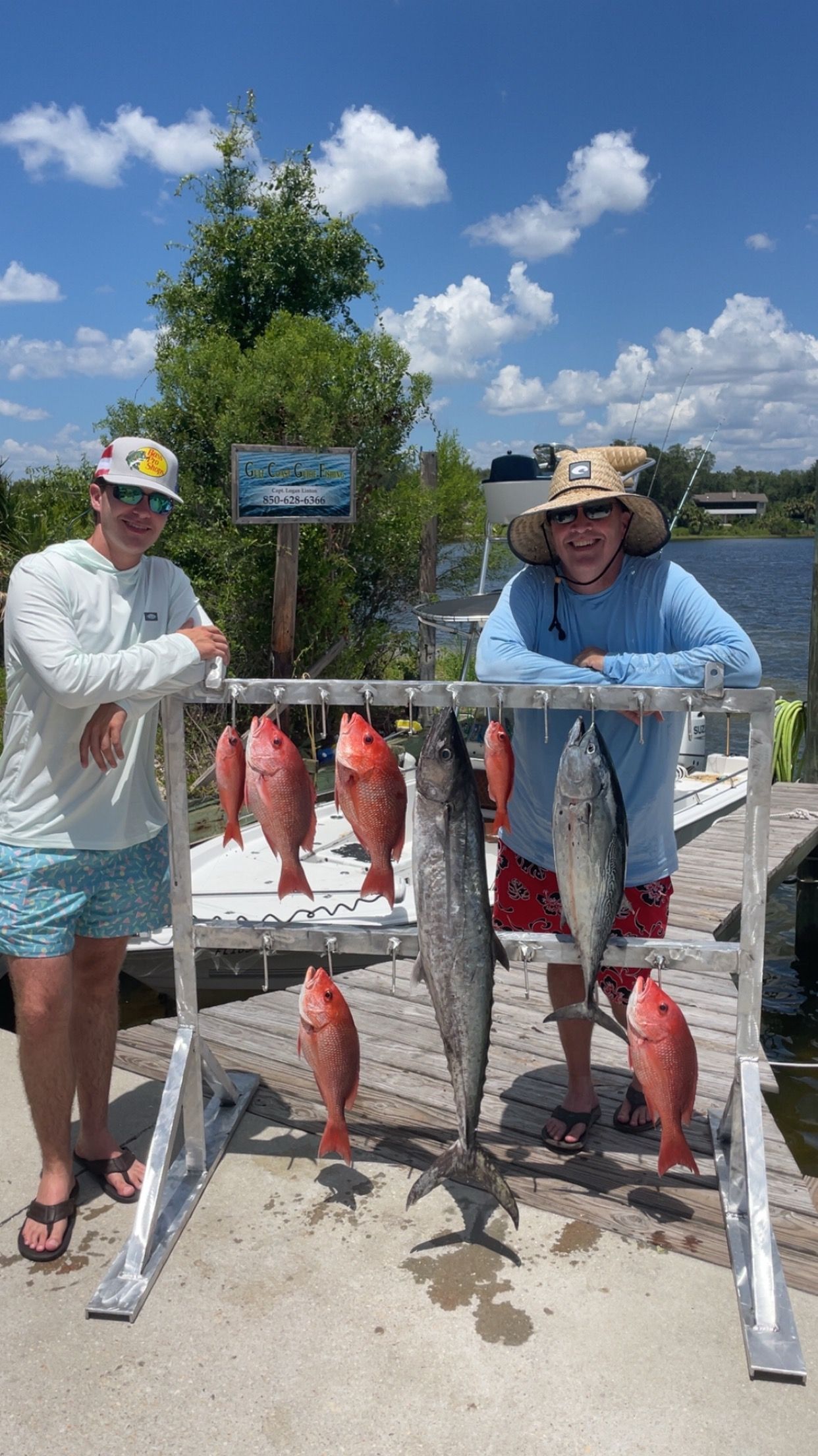 Two men with fishing catch displayed on a rack outdoors, sunny day.