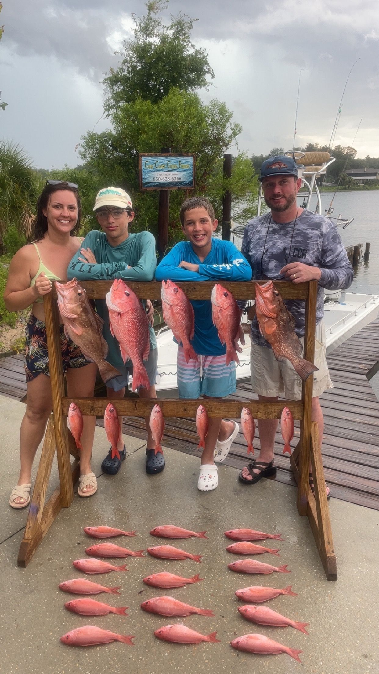 Family with many red fish they caught, smiling at the dock.
