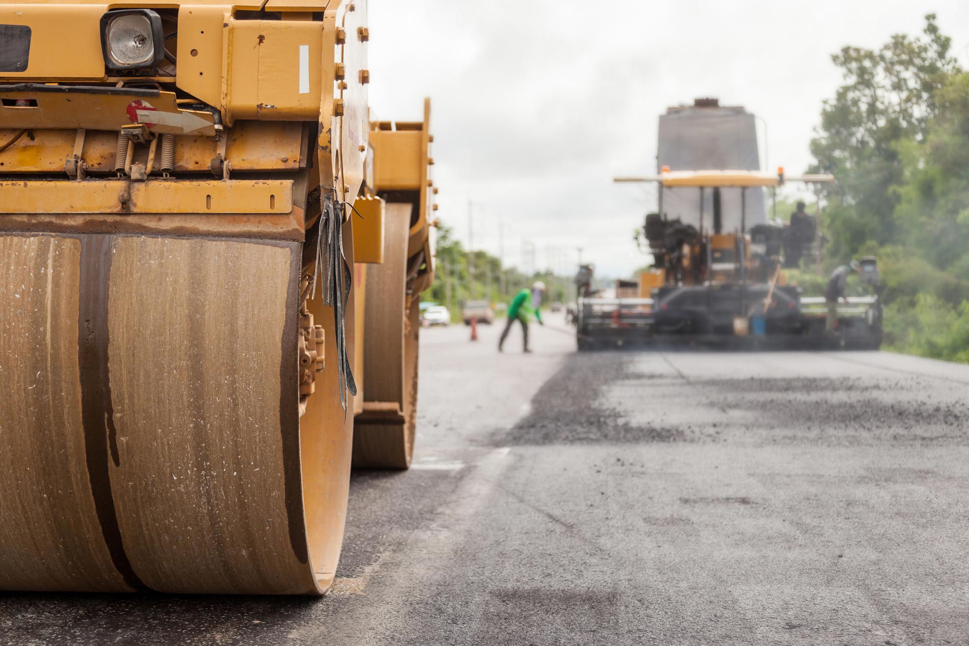 Road rollers paving asphalt on a road with workers in the distance