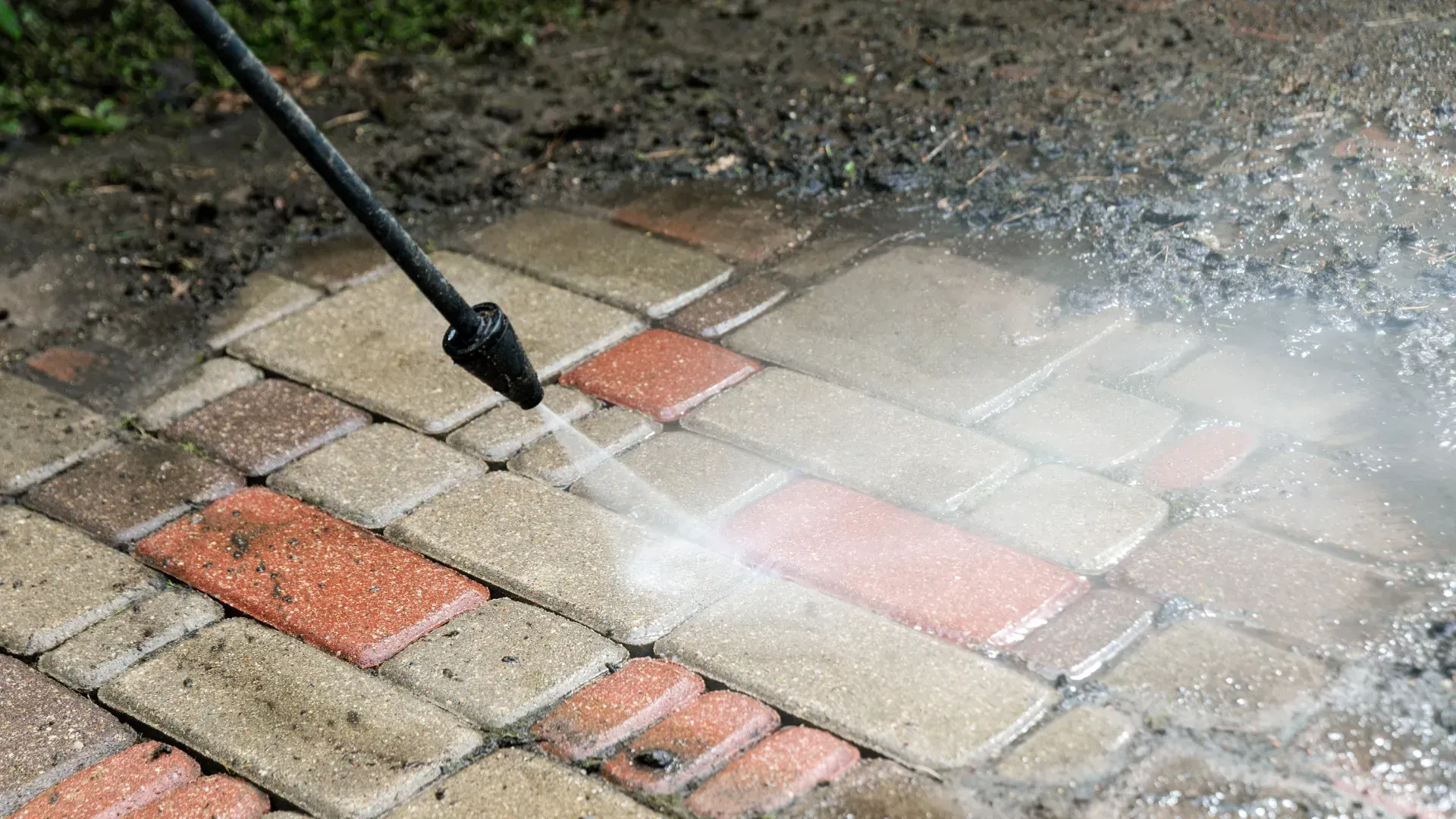 A person is using a high pressure washer to clean a brick walkway.
