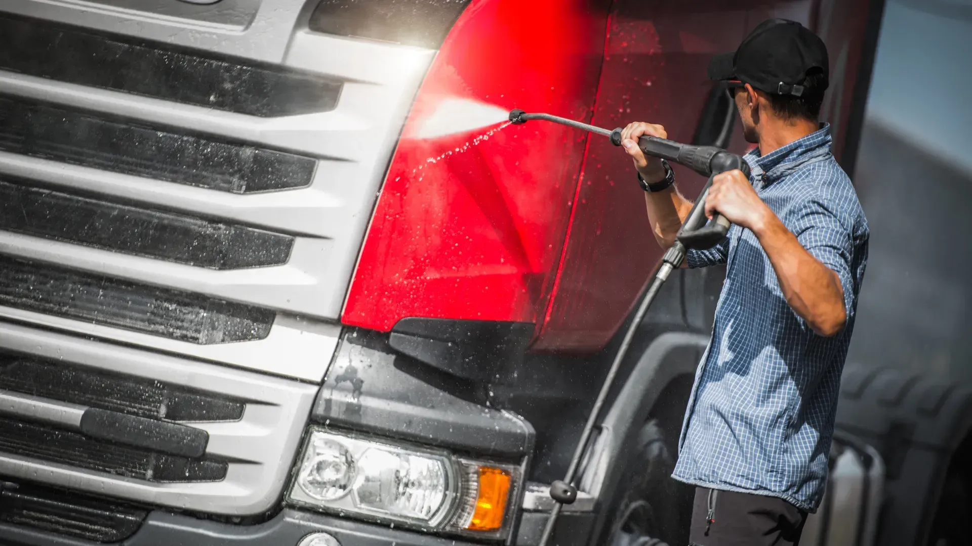 A man is washing a truck with a high pressure washer.