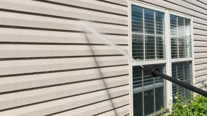 A person is cleaning the side of a house with a high pressure washer.
