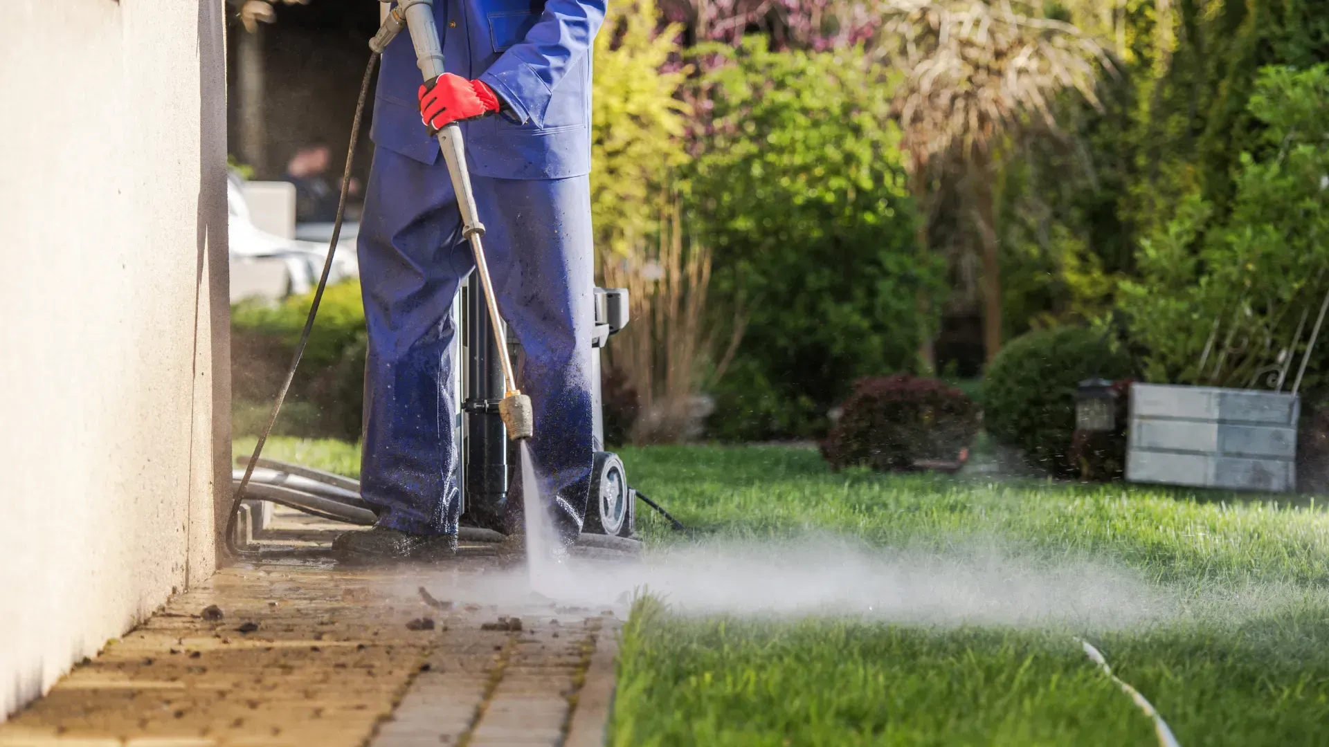 A man is using a high pressure washer to clean a sidewalk.
