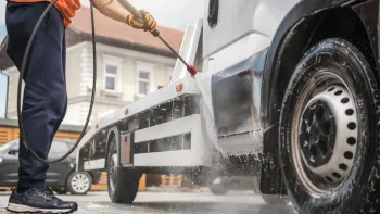 A man is washing a truck with a high pressure washer.