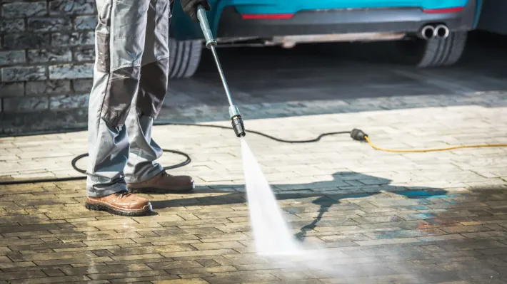 A man is using a high pressure washer to clean a driveway.