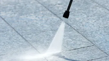 A person is using a high pressure washer to clean a tile floor.