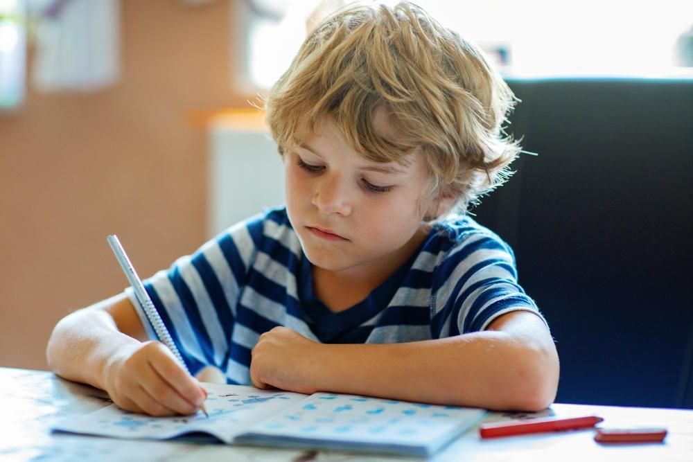 A Young Boy Is Sitting at A Table Writing — Oracle Psychology Child & Adolescent Psychologists Newcastle in Newcastle, NSW